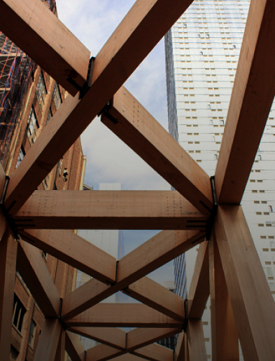 Wooden beam structure with intersecting grid pattern and a tall modern building in the background.